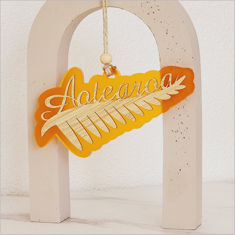 Vibrant orange acrylic ornament featuring a detailed silver fern design, perfect for holiday decor or unique gifts.