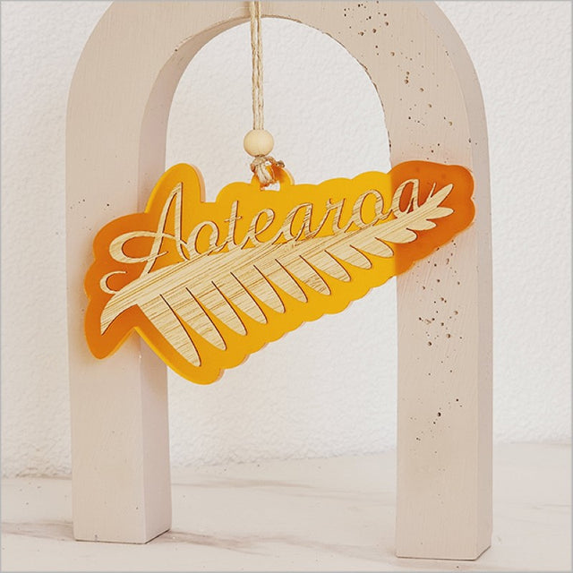 Vibrant orange acrylic ornament featuring a detailed silver fern design, perfect for holiday decor or unique gifts.