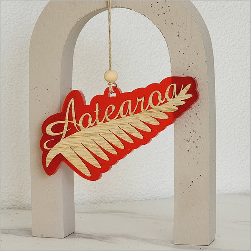 Red satin acrylic hanging ornament featuring an intricately laser-cut silver fern design, perfect for home decor or gifts.