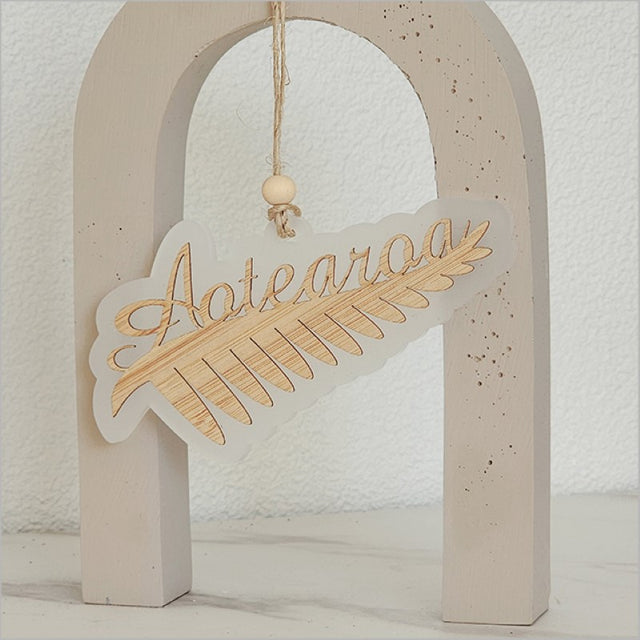 Hanging ornament featuring a silver fern design, crafted from white satin acrylic, ideal for festive decor and gifting.