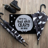 Humorous black doormat with "We're all bat shit crazy" text and full moon design for gothic-inspired decor.