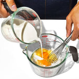 Clear glass measuring cup with easy-to-read markings, silicone lid, and non-slip handle for precise, mess-free pouring.