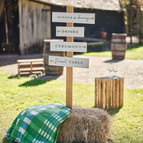 White wooden wedding signpost set with dark grey text, featuring signs for dinner, drinks, ceremony, and dessert table.