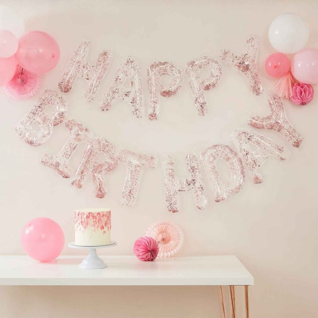 Clear foil letter balloons spelling 'Happy Birthday' with confetti, strung on rose gold twine, ideal for festive decor.