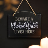 Whimsical "Beware a Wicked Witch Lives Here" sign, perfect for Halloween decor and inviting guests with a spooky charm.