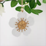 Elegant hanging ornament featuring laser-cut bamboo and white satin acrylic in the shape of a Manuka flower, perfect for festive decor.