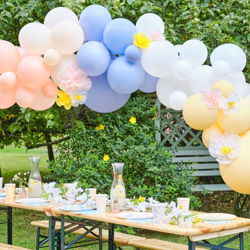 Pastel balloon arch with tissue paper flowers, perfect for spring events, featuring 60 balloons and eco-friendly assembly materials.