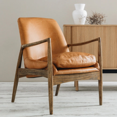 Armchair featuring cognac leather upholstery, duck feather cushions, and a sturdy smoked oak frame, blending Scandinavian and mid-century styles.