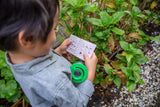 A child explores nature with the Bug Spotter Kit from Tiger Tribe, featuring a magnifying glass, net, and identification guide.