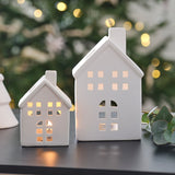 White ceramic house-shaped tealight holders, small and large, perfect for creating a cozy holiday ambiance.