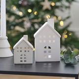 Charming white ceramic house-shaped tealight holders for a cozy winter ambiance, pack includes small and large sizes.