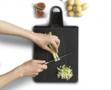 Folding black chopping board with non-slip feet and a handle for easy ingredient transfer and cleanup.