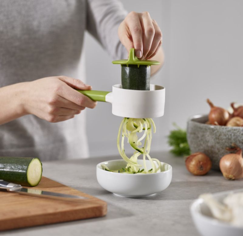 Joseph Joseph SpiroGo Compact Spiralizer in Green, featuring a long handle, stainless-steel blade, and safety finger guard.